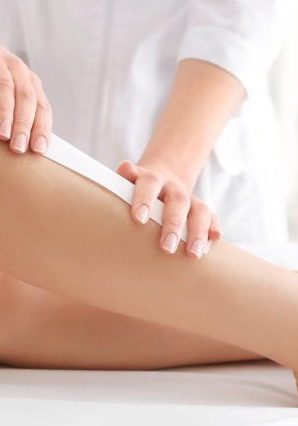 Beautician waxing female legs in spa center